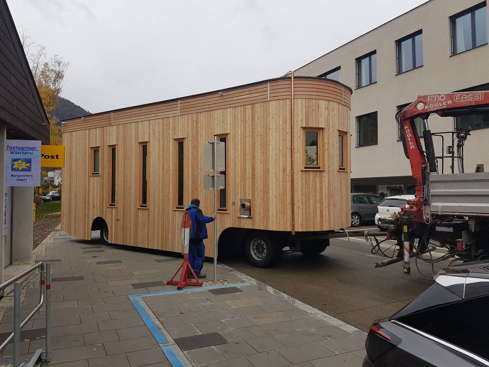 Der Wagon steht abgeladen zwischen Häusern, daneben der LKW mit ausgefahrenem Kran.