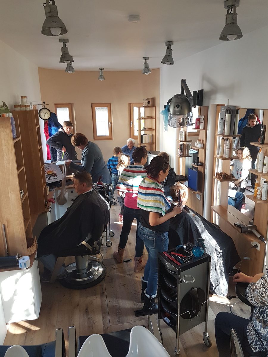 Mehrere Menschen sitzen und stehen im Salon, es wird gearbeitet.