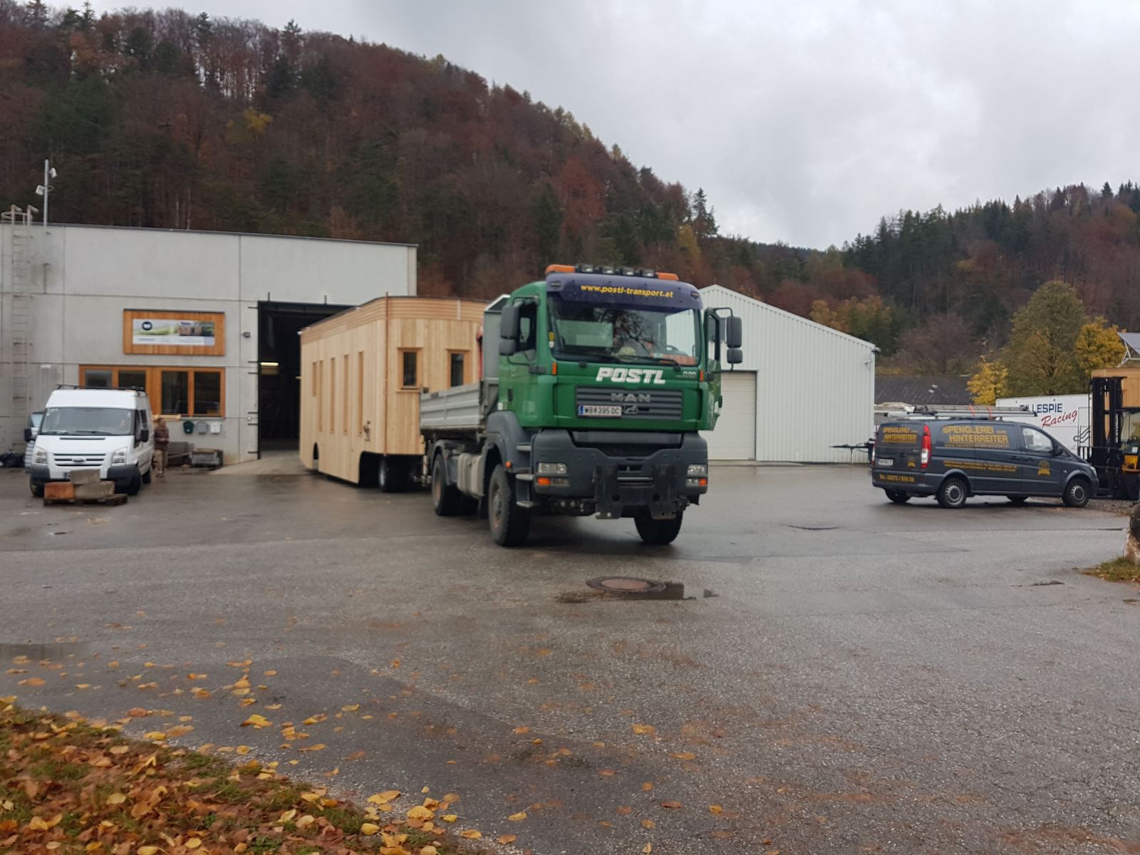 Der Wagon steht neben einem grünen LKW mit Ladekran auf dem Hof.