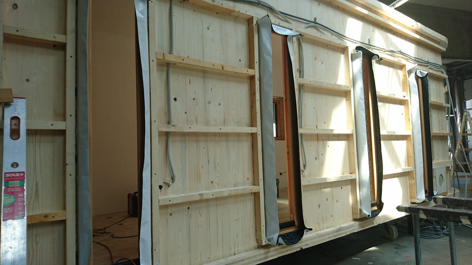 Eine Wand von innen: Ständer aus Holz, dazwischen verlegte Leitungen und eingesetzte Fenster.