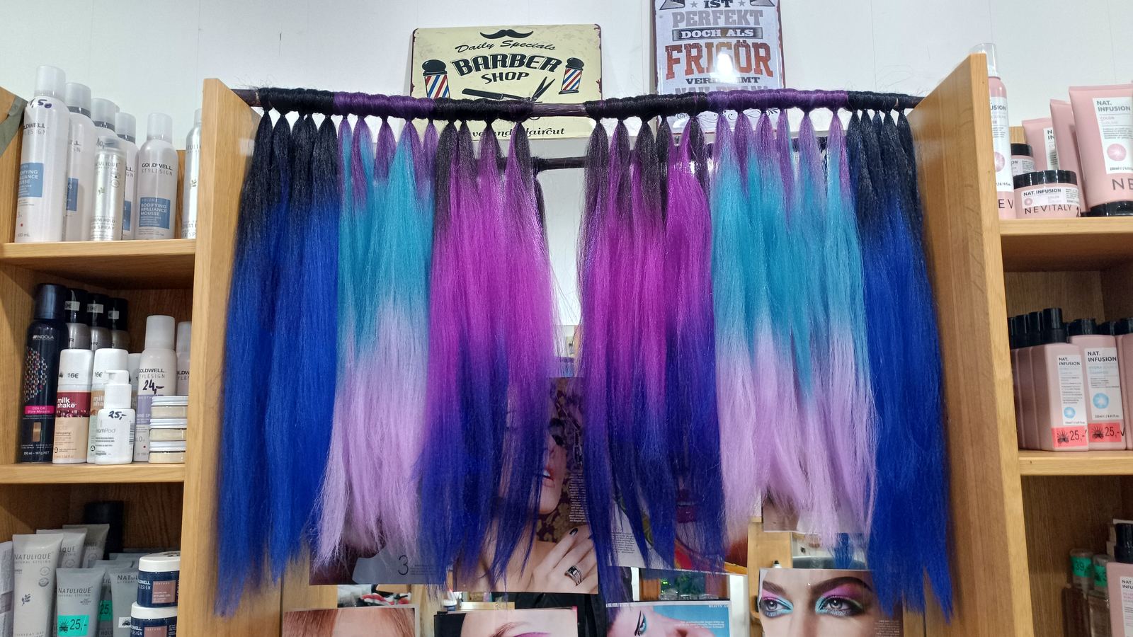 Ein Ständer mit Haarteilen in Violett, Blau und Pink im Salon, darunter Regale mit Produkten.
