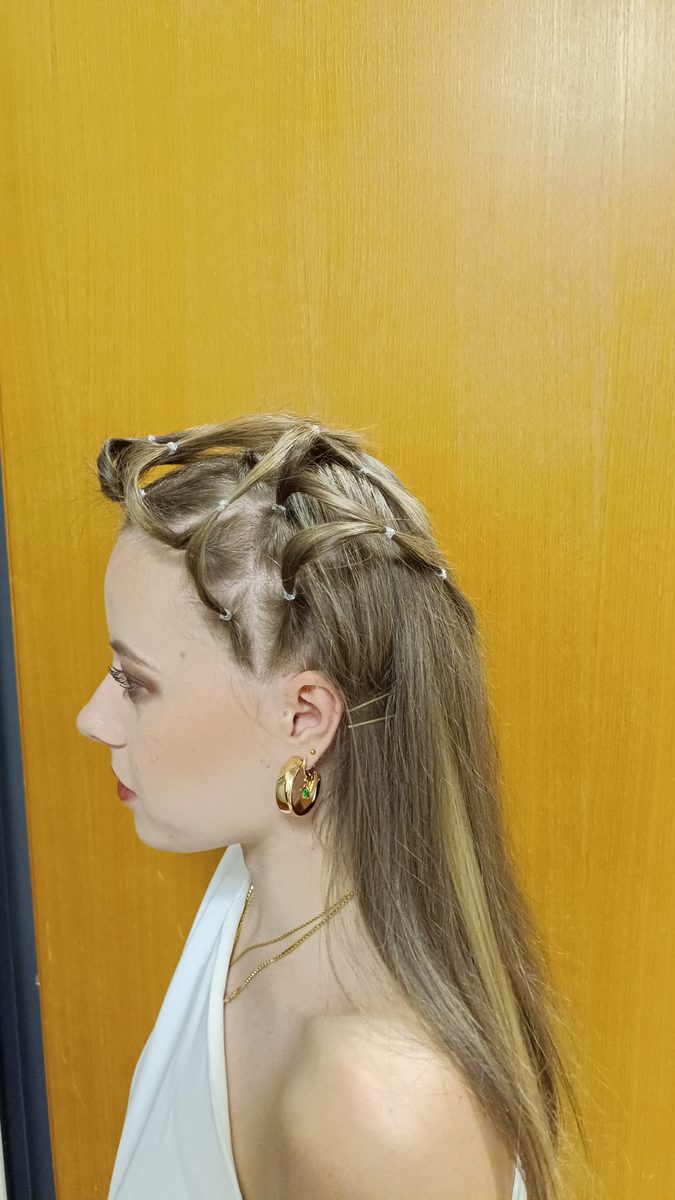 Langes blondes Haar, oben zu einem Zopf um den Kopf geflochten, unten offen.
