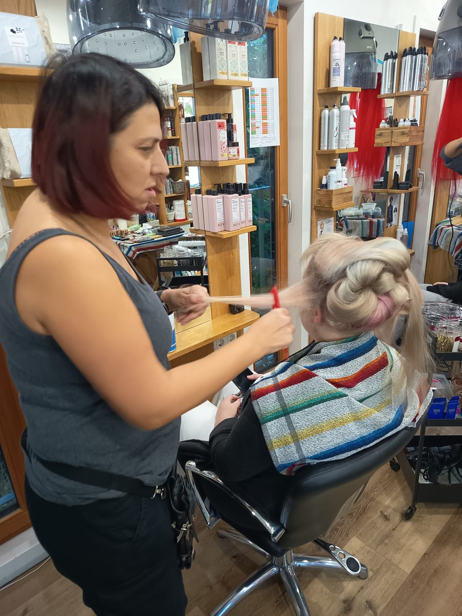 Sandra steckt einem Modell das blonde Haar hoch, im Hintergrund die Produktregale.