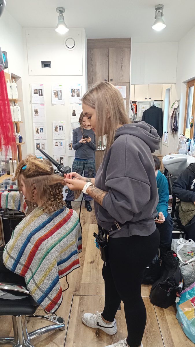 Eine Friseurin arbeitet am Morgen der Schau an den Haaren einer sitzenden Kundin.