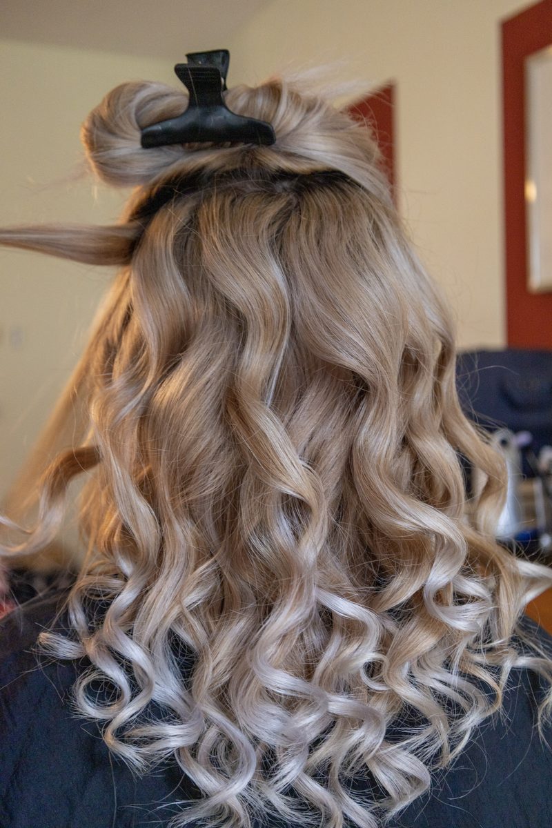 Lange blonde Locken fallen über den Rücken, das Deckhaar ist noch hochgesteckt.