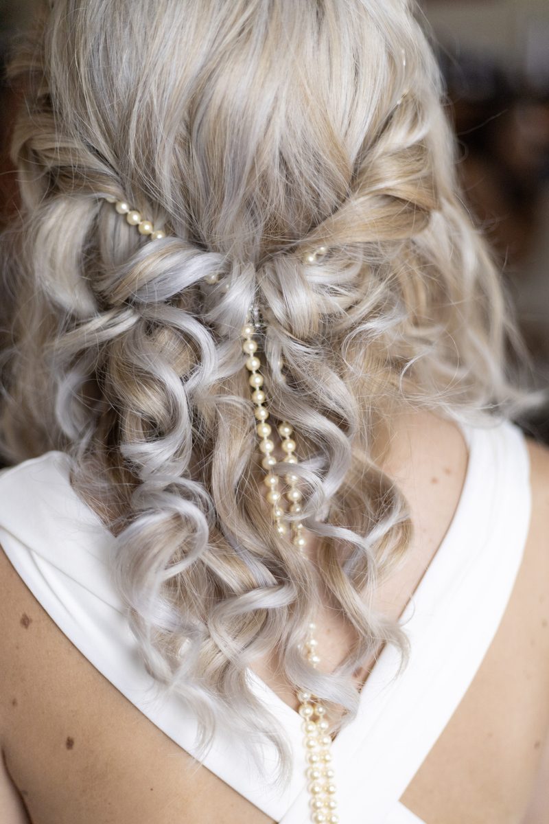 Silberblonde Locken, halb offen, mit einer langen Perlenkette durchzogen.