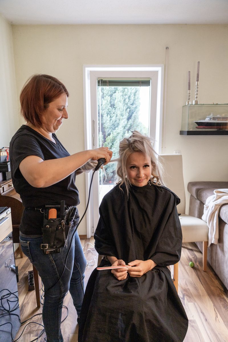 Sandra dreht einer sitzenden Kundin mit dem Lockenstab das Haar ein.
