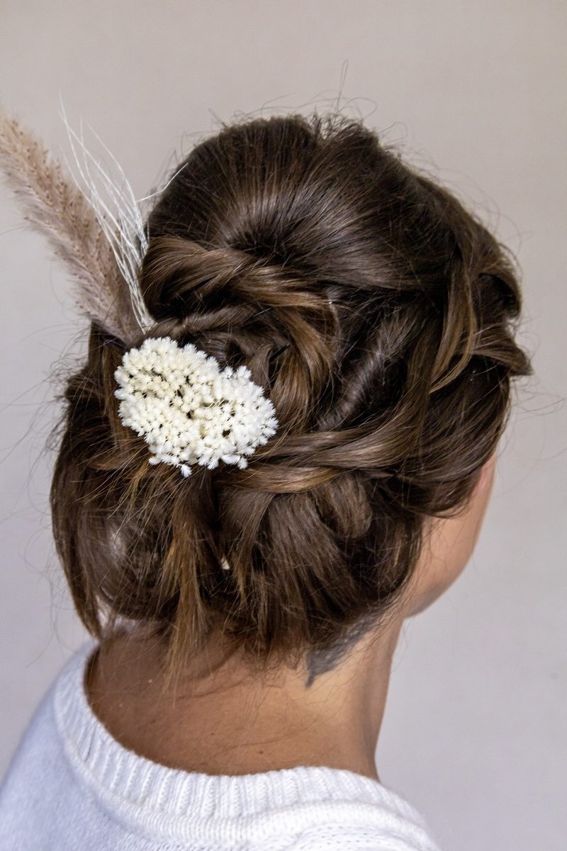Ein geflochtener Haarknoten mit Trockenblumen und Gräsern besteckt.
