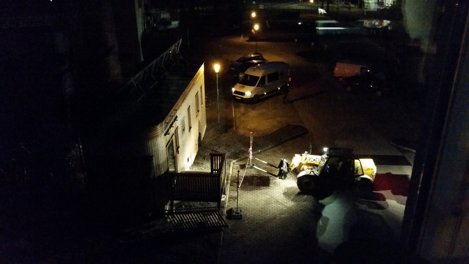 Der Platz bei Dunkelheit, der Wagon und die Fahrzeuge sind von Scheinwerfern angeleuchtet.