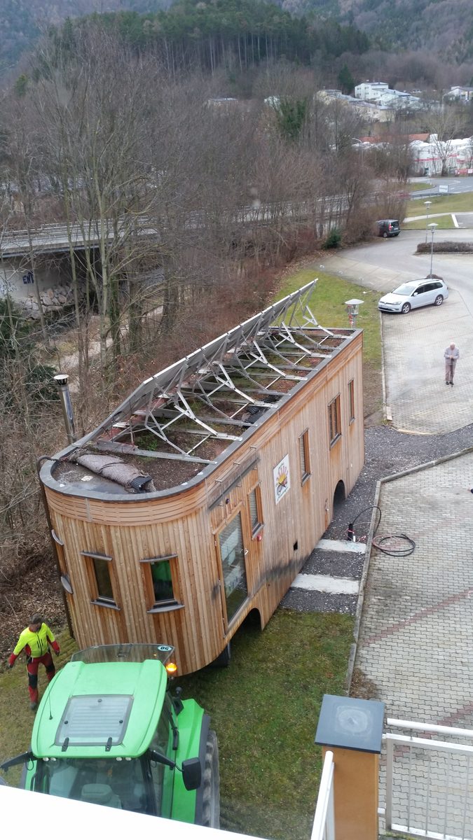 Der Wagon von der Seite auf dem Platz, davor der Traktor, das Solargestell ragt über das Dach.